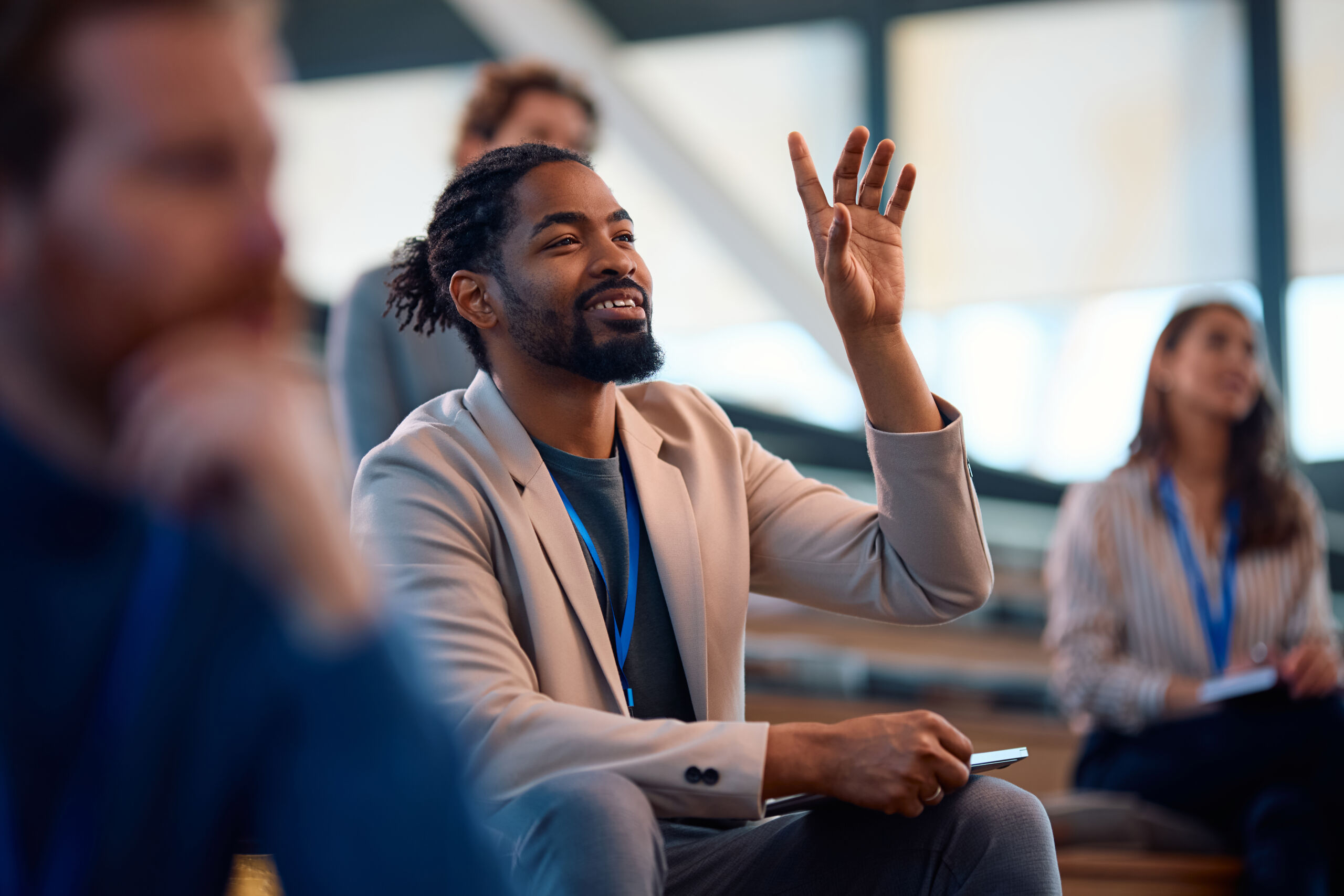 Happy black business seminar attendee asking a question from the audience. Entrepreneur raising his arm to ask a question during a business conference in board room.